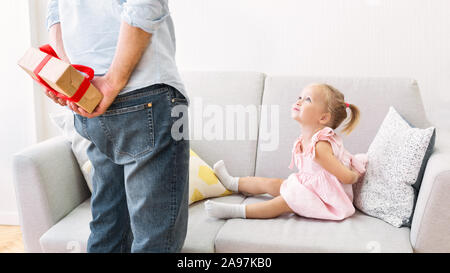 Papa se cacher cadeau d'anniversaire pour Fille derrière son dos, faisant de surprise pour cute little Girl. Panorama Banque D'Images