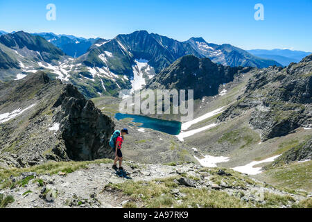 Une jeune femme avec un gros sac à dos randonnée vers un lac clair, bleu marine se cachant entre de hauts sommets de montagnes. Certaines des pentes sont couvertes de s Banque D'Images