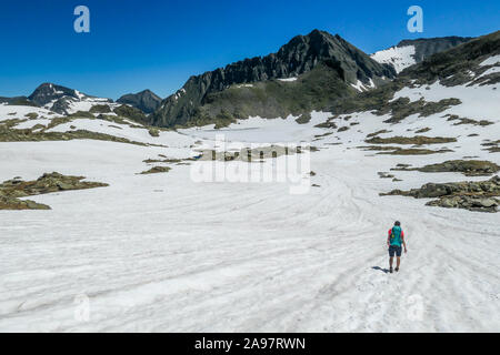 Une jeune femme avec un gros sac à dos, des randonnées à travers un plateau de neige en haute montagne. Fille, c'est portant des shorts.à l'arrière il y a un pic de montagne. Banque D'Images