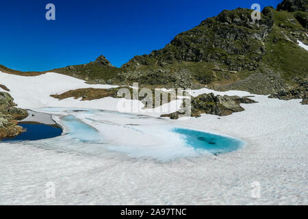 Vue sur un lac alpin congelé de glace. La glace brille dans beaucoup de différentes nuances de bleu. Lac est entouré de hautes montagnes. Il n'y a pas de neige au petit pois Banque D'Images