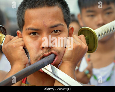 Les jeunes Chinois thaïlandais dévot taoïste (mah) Chanson perce les deux joues avec deux longues épées traditionnelles. Banque D'Images