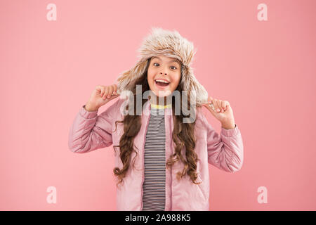 Sourire chaleureux. Bonne enfant fond rose. Vêtements chauds pour la saison froide. kid fashion trendy girl ressembler.. hipster style automne. L'activité de la petite enfance. fur hat earflap. accessoires petite fille winter hat. Banque D'Images