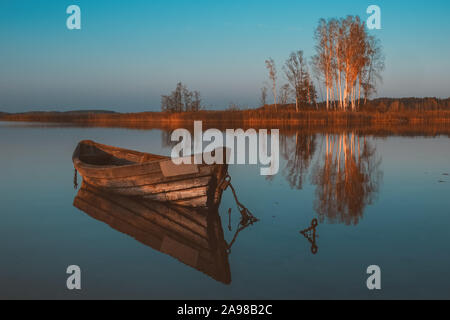 Bateau à rames en bois avec reflet dans un lac au crépuscule de l'eau encore sur paysage d'automne. Banque D'Images