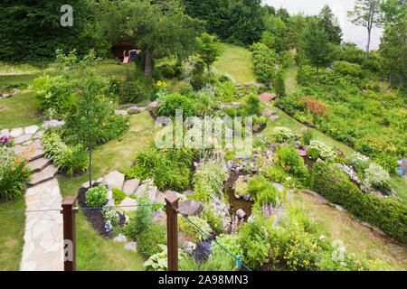 Vue de dessus de l'arrière-cour avec jardin résidentiel en pente bordée de roche orange bordé par cours d'hémérocalles hémérocalles - rose fleurs Astilbe, etc Banque D'Images