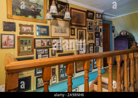 Des photographies anciennes et des dessins sur le mur au-dessus du bois d'érable escalier menant au rez-de-chaussée dans une ancienne maison de style cottage Canadiana 1835 Banque D'Images