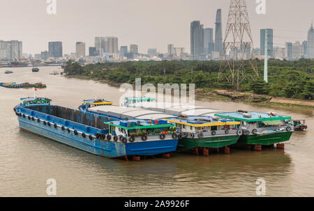 Ho Chi Minh Ville, Vietnam - 12 mars 2019 : chanson fleuve Sai Gon. Trois grandes barges moderne ancré dans l'eau brune. Ciel d'argent, ceinture verte et centre-ville Banque D'Images