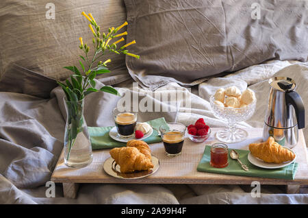 Petit-déjeuner romantique pour deux à l'intérieur d'une chambre à coucher. Cafetière et café verres, croissants, confiture, framboise et meringue sur bois fleurs romantique. Banque D'Images