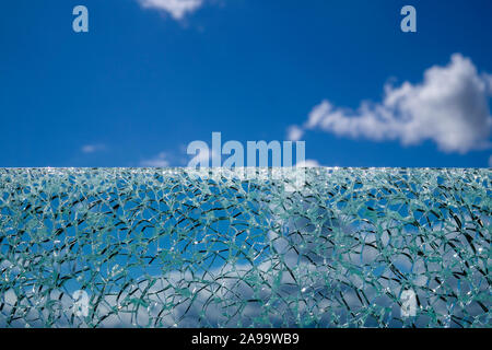 Surface en verre craquelé sur fond de ciel bleu à partir de l'angle faible, avec des nuages blancs flous en arrière-plan Banque D'Images