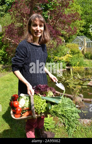 Dame avec un trug plein de légumes dans un jardin Banque D'Images