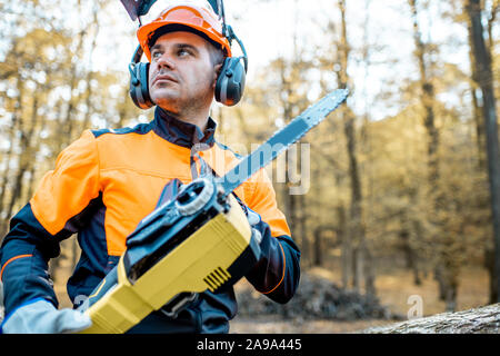 Portrait d'un bûcheron en vêtements de protection debout avec une tronçonneuse sur une pile de journaux dans la forêt Banque D'Images