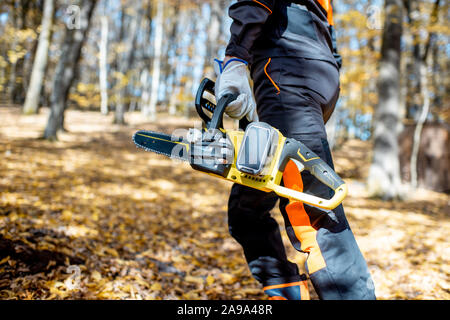 Vêtements de protection professionnels bûcheron en marchant avec une tronçonneuse dans la forêt, gros plan sur une scie Banque D'Images