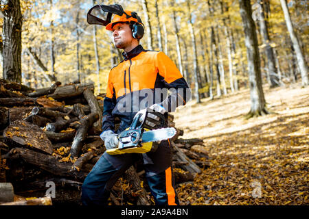 Portrait of a handsome bûcheron en vêtements de protection professionnelle avec une tronçonneuse dans la forêt Banque D'Images