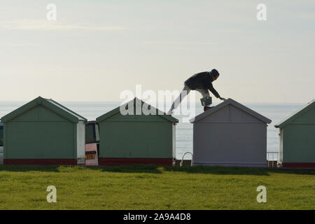 Un homme peindre le toit d'une cabane de plage sur la promenade de front de mer à Hove Lawns Banque D'Images