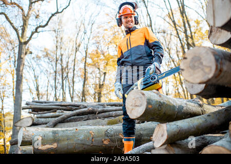 Portrait of a handsome bûcheron en vêtements de protection professionnelle avec une tronçonneuse près du sol en bois de sciage dans la forêt Banque D'Images