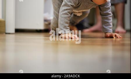 Toddler crawling sur plancher en bois chambre à coucher propre mère tout en regardant à l'arrière. Le développement de l'enfant et bébé grandissant. Banque D'Images