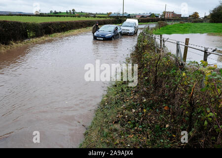 Bodenham, Herefordshire, UK - Jeudi 14 novembre 2019 - Un agriculteur de passage s'arrête pour aider une voiture coincée dans l'eau profonde sur une route rurale près du village de Bodenham après plus de pluie sont tombés sur les champs déjà saturé. Le passager est écoper l'eau de l'intérieur de la voiture. Photo Steven Mai / Alamy Live News Banque D'Images