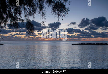 Un beau lever de soleil derrière les nuages avec le soleil tout casser sur l'horizon et encadré par un arbre à Cala Bona Majorque mer. Banque D'Images