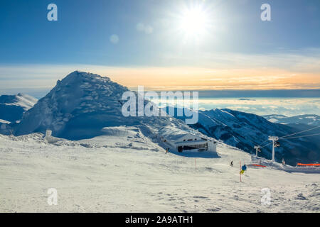 Les montagnes d'hiver. Les sommets enneigés et le brouillard dans les vallées. Grand soleil dans le ciel bleu sur la piste de ski. Ascenseur et bar de ski Banque D'Images