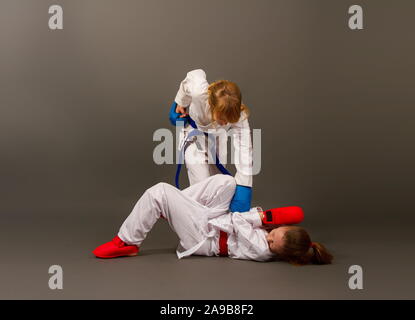 Deux petites filles en kimonos de karaté et de sports de plein d'équipement de protection rouge et bleu lutte contre un fond sombre Banque D'Images