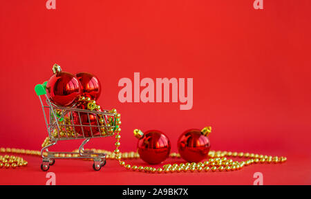 Boules de Noël cadeaux dans un chariot miniature et décorations sur un fond rouge. Noël et nouvel an noël, Vente boutique en ligne. Banque D'Images