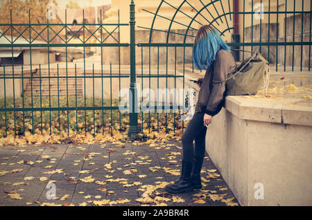 Emo girl de fumer et d'utiliser son téléphone dans la rue. Jeune étudiant avec les cheveux teints de couleur bleu Banque D'Images