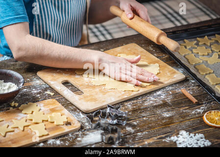 Une femme roule la pâte avec un rouleau à pâtisserie et le façonne avec ses mains pour une ambiance festive d'épices sur un fond de table en bois. Pour l'humeur de Noël Banque D'Images