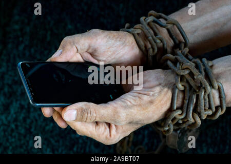 L'homme les mains liées avec chaîne métallique avec cadenas sur fond sombre suggérant internet ou la dépendance des médias sociaux Banque D'Images