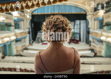 Une belle femme dans une robe seule sur le balcon d'un théâtre vide classique porte sur la scène et de l'intérieur Banque D'Images