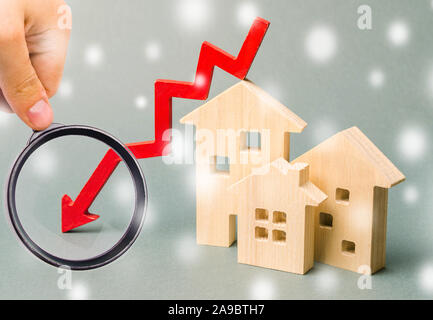 Maisons en bois miniature et flèche vers le bas. La notion de logement à faible demande. Des remises pour l'immobilier à l'hiver. Les taux d'intérêt hypothécaire. Cos bon marché Banque D'Images