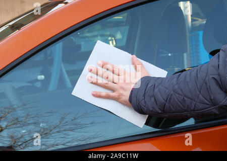 Après l'homme de verre lingettes lavage fenêtre avec une serviette en papier blanc. La main des hommes de corps de voiture et close up. Lavage de voiture à voiture Orange. Banque D'Images