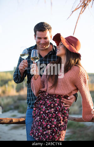 Couple amoureux buvant un verre de vin sur un ponton en bois par le bord d'un lac au coeur d'un grand vignoble. Banque D'Images