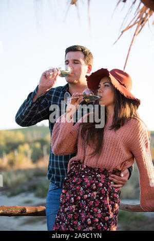 Couple in love boire du vin avec le coucher du soleil de la lumière derrière elle sur un ponton en bois dans une grande cour avec une vigne lake Banque D'Images