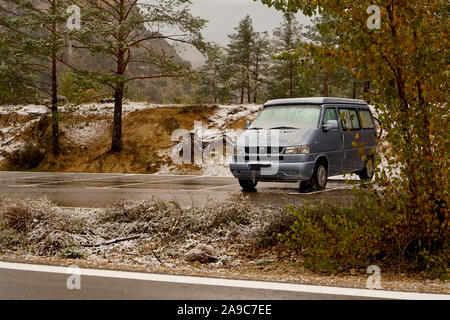 Un camping-car VW bleue garée à côté d'une réserve naturelle de forêt enneigée en hiver Banque D'Images