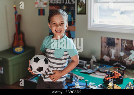 Smiling 5 yr old holding soccer ball dans chambre avec table de jeu LEGO Banque D'Images