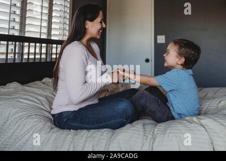 5 yr old boy et MI-30â€™maman avec de longs cheveux noirs laughing on bed Banque D'Images