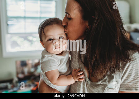 La Mi-40â€™embrassant bébé fille avec de grands yeux bruns en face de la fenêtre Banque D'Images