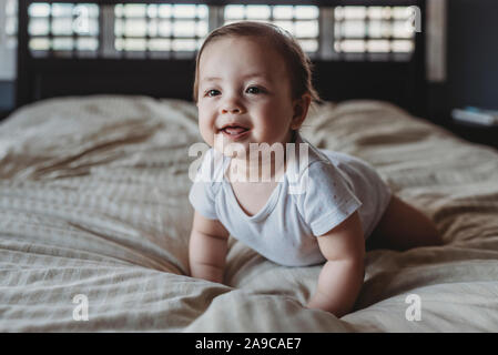 Bébé souriant avec deux dents ramper sur le lit à la lumière d'une fenêtre Banque D'Images