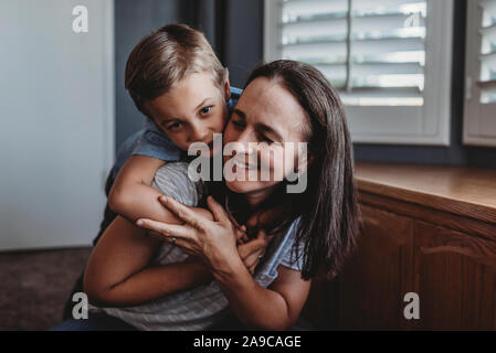 5 yr old boy hugging heureuse maman de l'arrière sur le plancher à côté de fenêtre Banque D'Images
