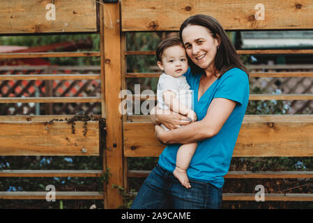 Mi-40's mère Smiling holding baby girl en plein air près de clôture en bois Banque D'Images