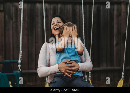 Jeune garçon sur swing avec rire maman couvre ses yeux Banque D'Images