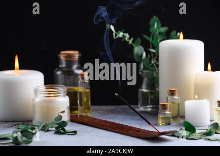 Bâton d'encens avec de la fumée sur pierre avec des bougies blanches et des huiles essentielles Banque D'Images