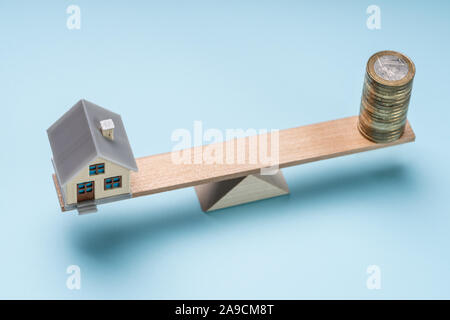 Une vue de dessus de miniature House et piles de pièces en bois sur Seesaw contre fond bleu Banque D'Images