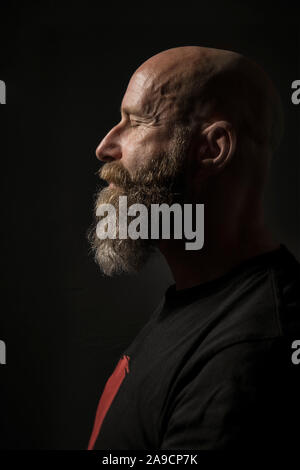 Une image d'un homme barbu aux yeux clos Vue de côté et un arrière-plan sombre Banque D'Images