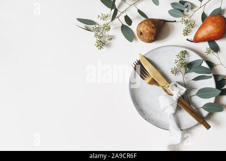 Tableau de l'action de l'automne place. Golden couverts, assiette de porcelaine, berry de feuilles d'eucalyptus et de branches, ruban de soie et de poire sur fond blanc Banque D'Images