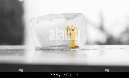 Jouet en caoutchouc jaune smiley congelé dans un cube de glace en train de fondre dans le soleil Banque D'Images