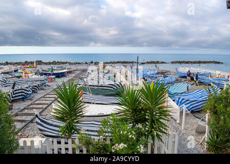 Ligne de bateaux de la plage de sable enveloppé en bleu et blanc couvre tôt le matin dans la ville balnéaire de Vintimille, Italie, sur la Riviera italienne. Banque D'Images