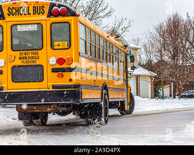 Un autobus scolaire jaune tourne un coin de rue de banlieue au début de l'hiver. La neige a récemment doublé la rue avec une poudre blanche. Banque D'Images