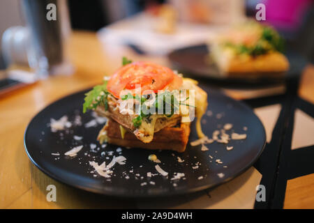 Les gaufres avec du bacon sandwich grillé et salade frech sur plaque noire. Arrière-plan de table en bois Banque D'Images