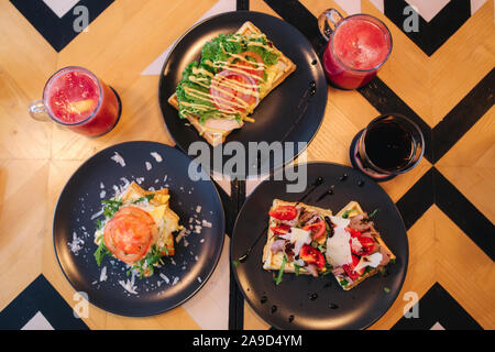 Les gaufres avec du bacon sandwich grillé et salade frech sur plaque noire. Arrière-plan de table en bois Banque D'Images