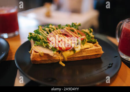 Les gaufres avec du bacon sandwich grillé et salade frech sur plaque noire. Arrière-plan de table en bois Banque D'Images